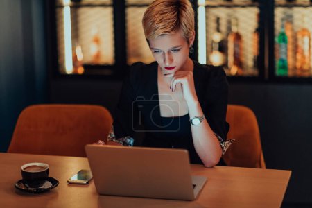 Téléchargez les photos : Femme d'affaires assis dans un café tout en se concentrant sur le travail sur un ordinateur portable et de participer à des réunions en ligne. Concentration sélective - en image libre de droit