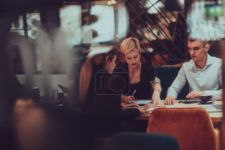 Photo for Photo through the glass of a group of business people sitting in a cafe and discussing business plans and ideas for new online commercial services. - Royalty Free Image