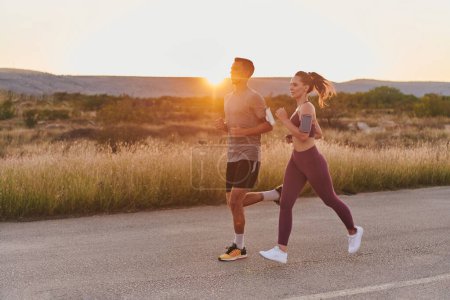 Photo for A handsome young couple running together during the early morning hours, with the mesmerizing sunrise casting a warm glow, symbolizing their shared love and vitality. - Royalty Free Image