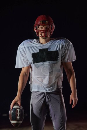 Foto de American Football Field: Lonely Athlete Warrior Standing on a Field sostiene su casco y listo para jugar. Jugador preparándose para correr, atacar y anotar touchdown - Imagen libre de derechos