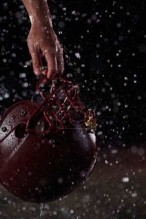 Photo for Close up of American Football Athlete Warrior Standing on a Field focus on his Helmet and Ready to Play. Player Preparing to Run, Attack and Score Touchdown. Rainy Night with Dramatic lens flare. - Royalty Free Image