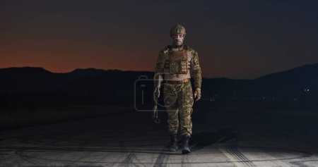 Photo for A professional soldier in full military gear striding through the dark night as he embarks on a perilous military mission. - Royalty Free Image
