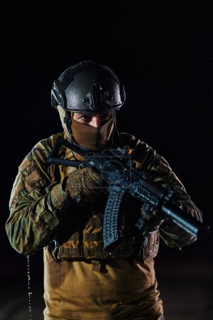 Foto de Un soldado profesional en equipo militar completo caminando a través de la noche oscura mientras se embarca en una peligrosa misión militar. - Imagen libre de derechos
