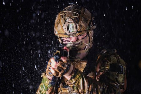 Foto de Soldado del ejército en uniformes de combate con un rifle de asalto, portaplatos y casco de combate que va en una misión peligrosa en una noche lluviosa - Imagen libre de derechos