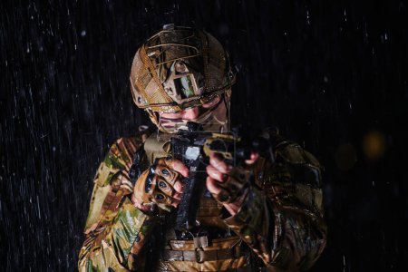 Photo for Army soldier in Combat Uniforms with an assault rifle, plate carrier and combat helmet going on a dangerous mission on a rainy night - Royalty Free Image