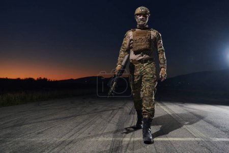 Foto de Un soldado profesional en equipo militar completo caminando a través de la noche oscura mientras se embarca en una peligrosa misión militar. - Imagen libre de derechos