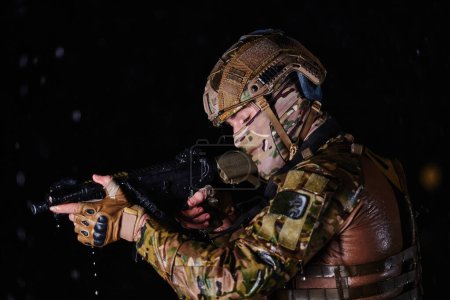 Photo for Army soldier in Combat Uniforms with an assault rifle, plate carrier and combat helmet going on a dangerous mission on a rainy night - Royalty Free Image
