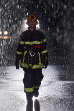 Photo for A determined female firefighter in a professional uniform striding through the dangerous, rainy night on a daring rescue mission, showcasing her unwavering bravery and commitment to saving lives - Royalty Free Image