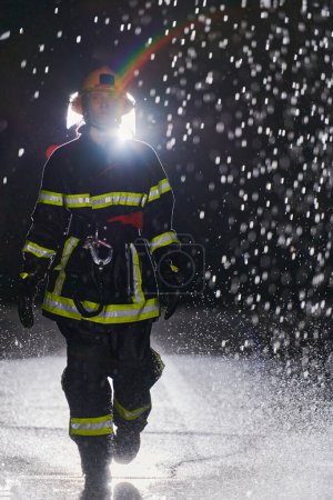 Foto de Una decidida bombera con un uniforme profesional que camina a través de la peligrosa y lluviosa noche en una atrevida misión de rescate, mostrando su valentía inquebrantable y su compromiso de salvar vidas. - Imagen libre de derechos