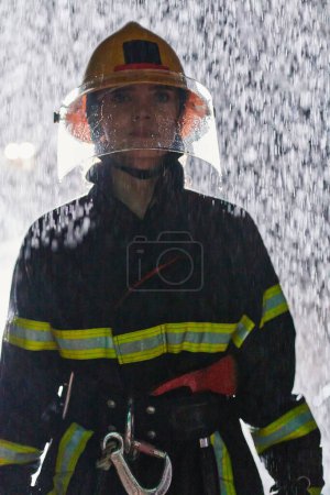 Téléchargez les photos : Une pompière déterminée portant un uniforme professionnel traversant la dangereuse nuit pluvieuse dans le cadre d'une mission de sauvetage audacieuse, montrant sa bravoure inébranlable et son engagement à sauver des vies - en image libre de droit