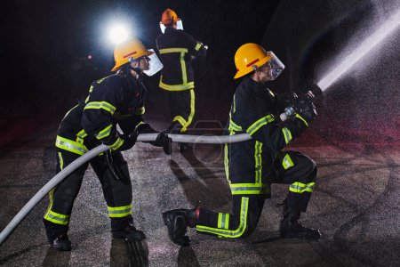 Foto de Bomberos que utilizan una manguera de agua para eliminar un peligro de incendio. Equipo de bomberos femeninos y masculinos en misión de rescate peligrosa - Imagen libre de derechos