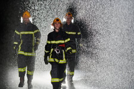 Téléchargez les photos : Un groupe de pompiers professionnels marchant dans la nuit pluvieuse en mission de sauvetage, leurs pas déterminés et leurs expressions intrépides reflétant leur bravoure inébranlable et inébranlable - en image libre de droit