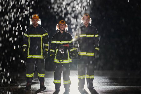 Foto de Un grupo de bomberos profesionales marchando a través de la noche lluviosa en una misión de rescate, sus pasos decididos y sus expresiones intrépidas que reflejan su valentía inquebrantable e inquebrantable - Imagen libre de derechos