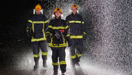Téléchargez les photos : Un groupe de pompiers professionnels marchant dans la nuit pluvieuse en mission de sauvetage, leurs pas déterminés et leurs expressions intrépides reflétant leur bravoure inébranlable et inébranlable - en image libre de droit