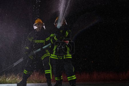 Téléchargez les photos : Les pompiers utilisant un tuyau d'eau pour éliminer un risque d'incendie. Équipe de pompiers féminins et masculins en mission de sauvetage dangereuse - en image libre de droit