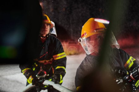 Téléchargez les photos : Les pompiers utilisant un tuyau d'eau pour éliminer un risque d'incendie. Équipe de pompiers féminins et masculins en mission de sauvetage dangereuse - en image libre de droit