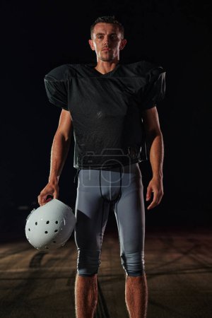 Téléchargez les photos : American Football Field : Solitaire athlète guerrier debout sur un terrain tient son casque et prêt à jouer. Joueur se préparant à courir, attaquer et marquer Touchdown - en image libre de droit