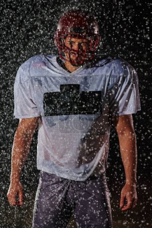 Photo for American Football Field: Lonely Athlete Warrior Standing on a Field Holds his Helmet and Ready to Play. Player Preparing to Run, Attack and Score Touchdown. Rainy Night with Dramatic Fog, Blue Light. - Royalty Free Image