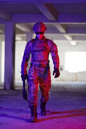Téléchargez les photos : Un soldat professionnel entreprend une mission périlleuse dans un bâtiment abandonné illuminé par des néons bleus et violets. - en image libre de droit