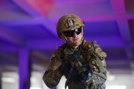 Foto de Un soldado profesional emprende una peligrosa misión en un edificio abandonado iluminado por luces azul neón y púrpura. - Imagen libre de derechos