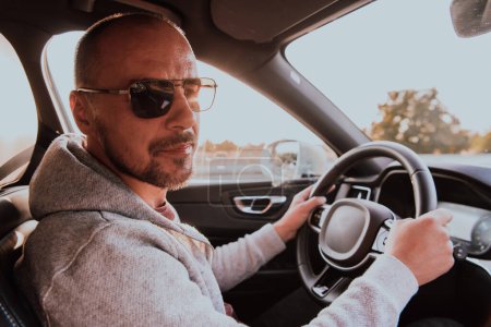 Foto de Un hombre con gafas de sol conduciendo un coche al atardecer. El concepto de viaje en coche. - Imagen libre de derechos