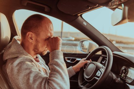 Foto de Un conductor cansado sosteniendo su cabeza. Conductor cansado y agotado conduciendo un coche al atardecer. - Imagen libre de derechos