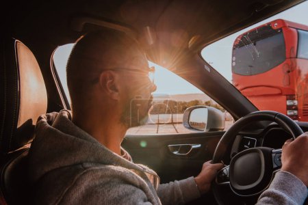 Téléchargez les photos : Un homme avec des lunettes de soleil conduisant une voiture au coucher du soleil. Le concept de voyage en voiture. - en image libre de droit