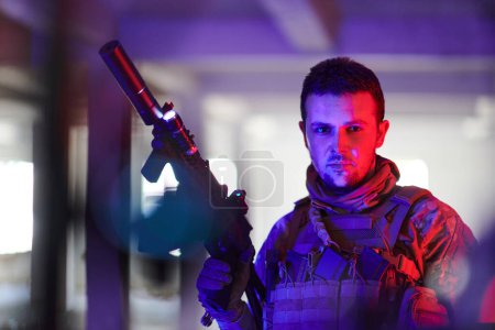Photo for A professional soldier undertakes a perilous mission in an abandoned building illuminated by neon blue and purple lights. - Royalty Free Image