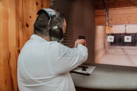 Photo for A man practices shooting a pistol in a shooting range while wearing protective headphones. - Royalty Free Image