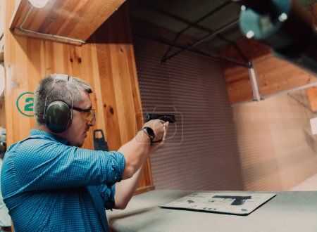 Foto de Un hombre practica disparar una pistola en un campo de tiro mientras usa auriculares protectores. - Imagen libre de derechos