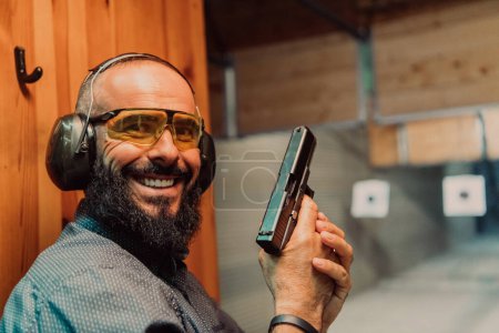 Foto de Un hombre practica disparar una pistola en un campo de tiro mientras usa auriculares protectores. - Imagen libre de derechos