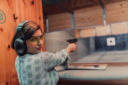 Foto de Una mujer practica disparar una pistola en un campo de tiro mientras usa auriculares protectores. - Imagen libre de derechos