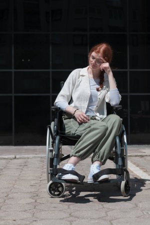 Foto de Frente a un moderno edificio corporativo, una joven sentada en una silla de ruedas con confianza, que simboliza el empoderamiento, la inclusión y la fuerza para superar los desafíos en el mundo de los negocios. - Imagen libre de derechos