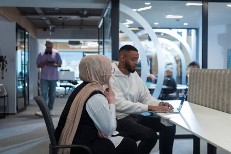 Téléchargez les photos : Dans un bureau moderne, un homme d'affaires afro-américain et son collègue musulman, portant un hijab, s'engagent dans des discussions collaboratives, abordent diverses tâches commerciales et résolvent des problèmes. - en image libre de droit
