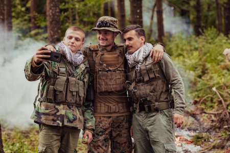 Téléchargez les photos : Équipe de soldats et terroristes prenant selfie avec smartphone dans la forêt. - en image libre de droit