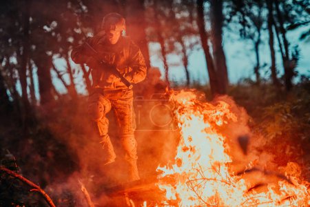 Foto de Soldado en acción por la noche en la zona forestal. Misión militar nocturna saltando sobre el fuego. - Imagen libre de derechos