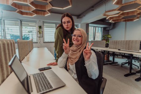 Foto de Jóvenes empresarias, una de ellas con un hijab, están colaborando en la resolución de problemas en una oficina moderna mientras trabajan en una computadora portátil, ejemplificando la diversidad, profesionalidad y trabajo en equipo. - Imagen libre de derechos