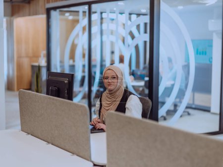 Téléchargez les photos : Dans un bureau moderne, une jeune entrepreneure musulmane portant un hijab travaille avec confiance et diligence sur son ordinateur, incarnant détermination, créativité et autonomisation dans le monde des affaires. - en image libre de droit