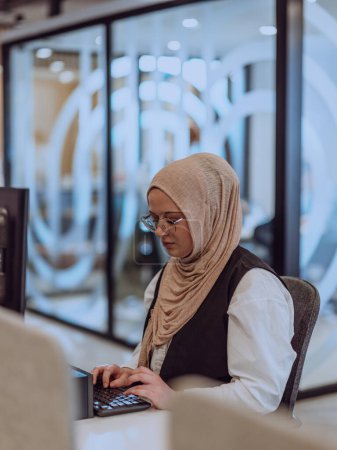 Photo for In a modern office, a young Muslim entrepreneur wearing a hijab sits confidently and diligently works on her computer, embodying determination, creativity, and empowerment in the business world - Royalty Free Image