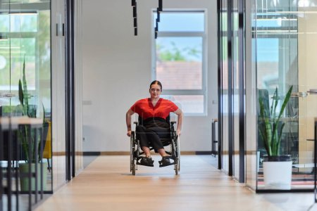 Foto de Una joven empresaria moderna en silla de ruedas está rodeada por un espacio de trabajo inclusivo con oficinas con paredes de cristal, que encarna la determinación y la innovación en el mundo empresarial. - Imagen libre de derechos
