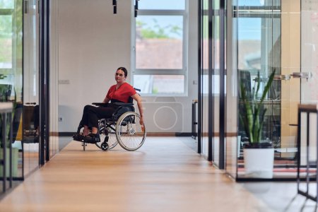 Photo for A modern young businesswoman in a wheelchair is surrounded by an inclusive workspace with glass-walled offices, embodying determination and innovation in the business world. - Royalty Free Image