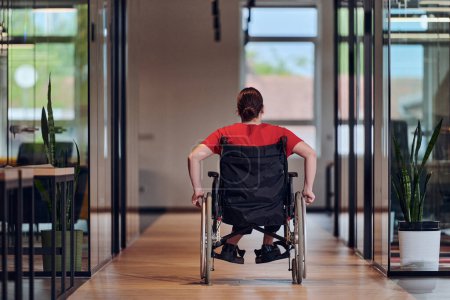 Foto de Una joven empresaria moderna en silla de ruedas está rodeada por un espacio de trabajo inclusivo con oficinas con paredes de cristal, que encarna la determinación y la innovación en el mundo empresarial. - Imagen libre de derechos