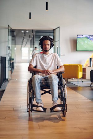 Foto de Un hombre de negocios en silla de ruedas ocupa un pasillo dentro de un moderno centro de coworking de startups, incorporando inclusividad y determinación en el entorno empresarial. - Imagen libre de derechos
