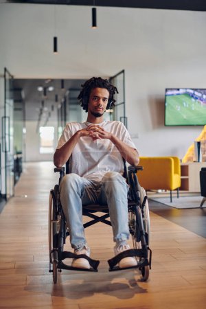 Foto de Un hombre de negocios en silla de ruedas ocupa un pasillo dentro de un moderno centro de coworking de startups, incorporando inclusividad y determinación en el entorno empresarial. - Imagen libre de derechos