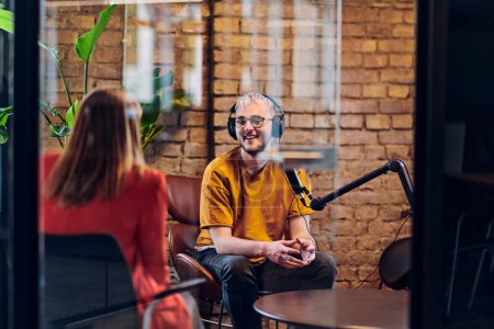 Photo for A gathering of young business professionals, some seated in a glass-walled office, engage in a lively conversation and record an online podcast, embodying modern collaboration and dynamic interaction - Royalty Free Image