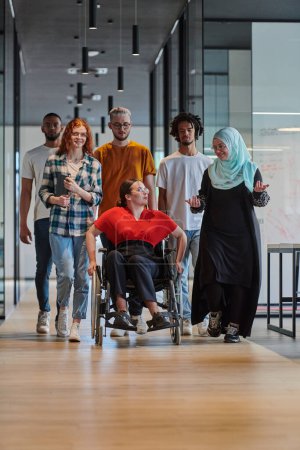 Photo for A diverse group of young business people walking a corridor in the glass-enclosed office of a modern startup, including a person in a wheelchair and a woman wearing a hijab, showing a dynamic mix of - Royalty Free Image