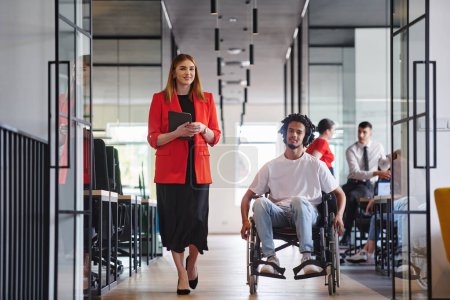 Photo for A group of young business people in a modern glass-walled office captures the essence of diversity and collaboration, while two colleagues, including an African American businessman in a wheelchair - Royalty Free Image