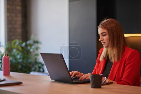 Photo for In a contemporary office setting, a young businesswoman is focused on her laptop, displaying dedication and efficiency in her work. - Royalty Free Image