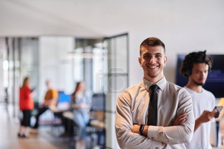 Téléchargez les photos : Un jeune chef d'entreprise se tient les bras croisés dans un couloir de bureau moderne, rayonnant de confiance et d'un sens de l'objectif, incarnant une présence dynamique et inspirante - en image libre de droit