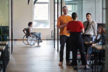 Photo for A diverse group of colleagues engages in a discussion about business challenges within a modern coworking startup center, while in the background, their wheelchair-bound colleague symbolizes - Royalty Free Image